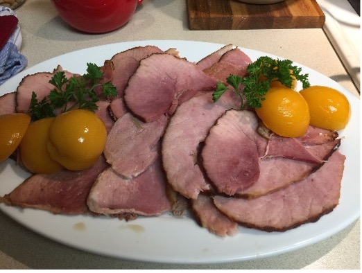 Sliced baked ham on a serving platter garnished with peaches