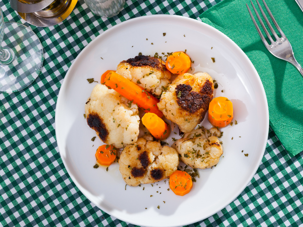 Roasted cauliflower and carrots on a white plate. The cauliflower florets are lightly browned and caramelized, while the carrots are tender and slightly charred. The dish is sprinkled with fresh parsley.