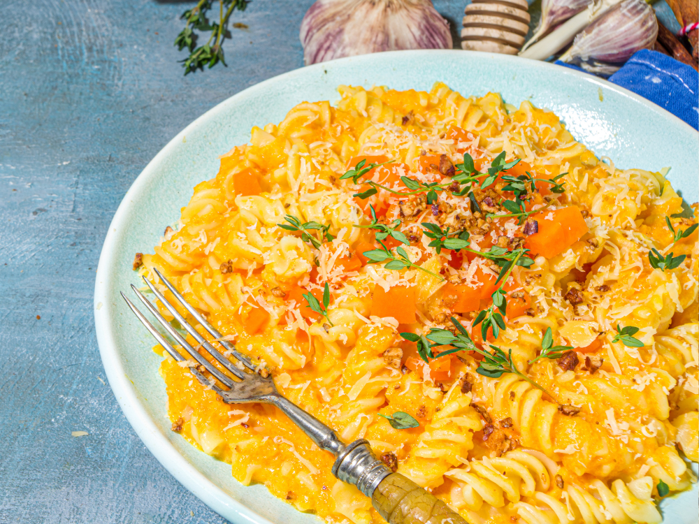 A plate of pasta with a creamy pumpkin sauce, garnished with fresh herbs and grated Parmesan cheese.