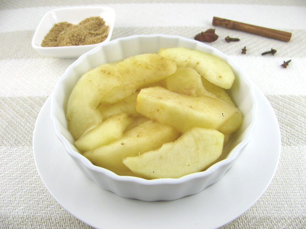 A bowl of golden brown stewed apples, with a sprinkle of cinnamon on top.