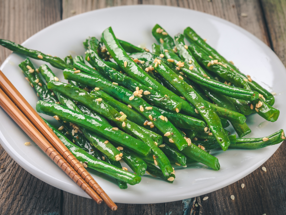 A plate of green beans tossed in a ginger sesame sauce, garnished with sesame seeds.