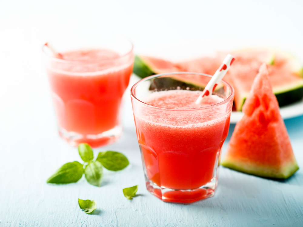 Two refreshing Hydrating Watermelon Slushes in glasses with fresh watermelon slices on a wooden table.