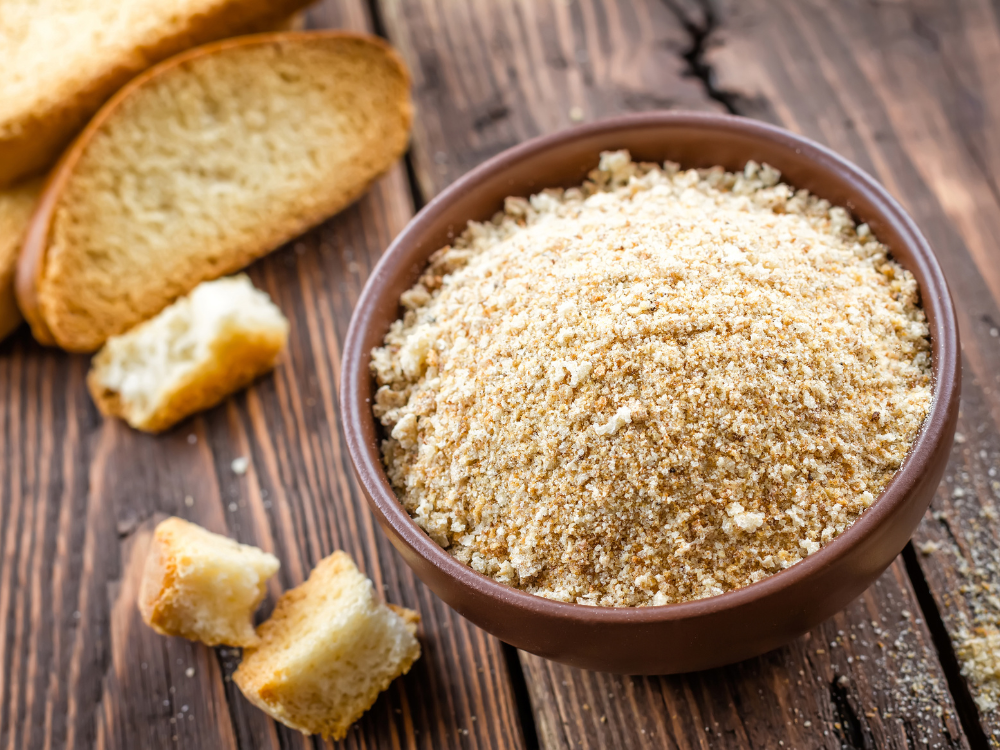 A bowl full of breadcrumbs. The breadcrumbs are golden brown and have a slightly uneven texture.