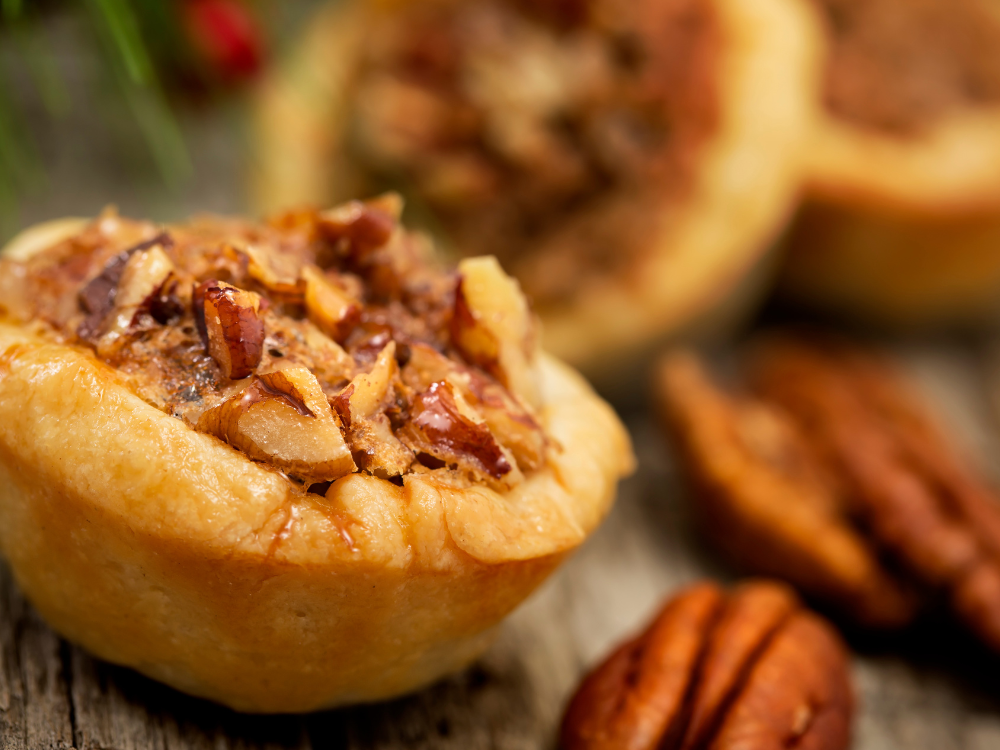 Close-up view of bite-sized pecan tassies, a type of pastry. Each tassie features a golden brown crust filled with a mixture of chopped pecans, sugar, and butter.
