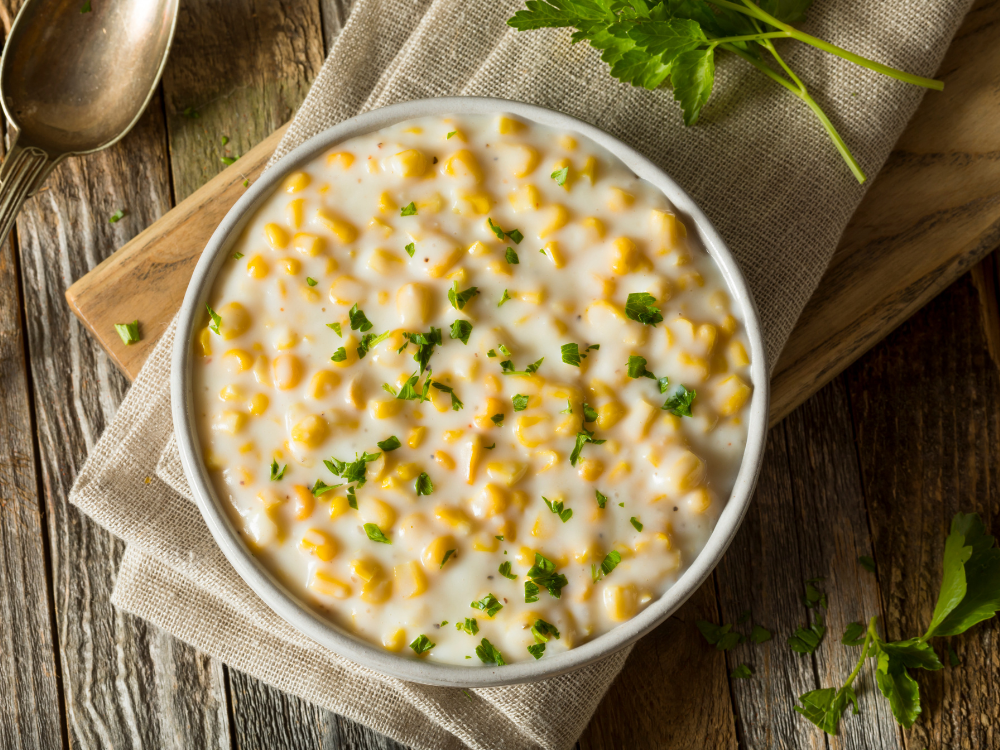 A bowl of creamy yellow corn with swirls of coconut milk on top and sprinkled with herbs and spices.